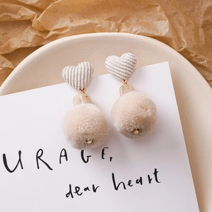 Détail de boucles d'oreilles d'hiver avec cœurs en tissu beige et pompons marron doux