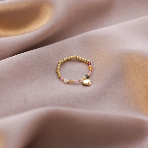 Detail of beaded elastic ring with colorful gems and gold heart charm on pink silk