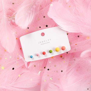 Macro shot of colorful matte sphere stud earrings set on decorative pink feather background