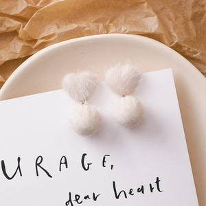 Détail de boucles d'oreilles cœur en peluche avec pompons en fausse fourrure beige