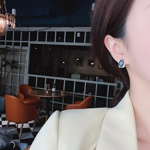 Close-up of blue rectangular gemstone stud earring with gold frame worn by a model