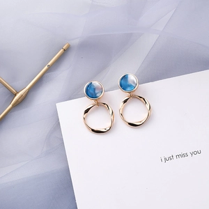 Detail of elegant gold earrings with blue marble texture inlays on a white card