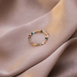 Macro shot of colorful beaded stretch ring with faceted crystals on soft pink satin fabric