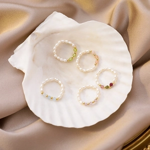 Detailed view of handmade pearl rings with colorful crystals on elegant silk and shell