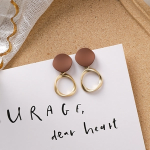 Détail de boucles d'oreilles marron chocolat avec anneaux dorés mats sur fond de liège