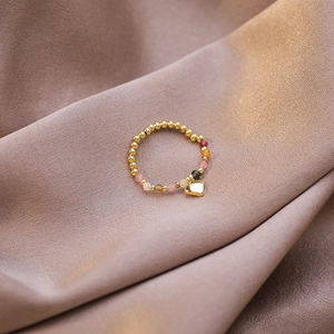 Detail of beaded stretch ring with colorful crystals and golden heart pendant on silk