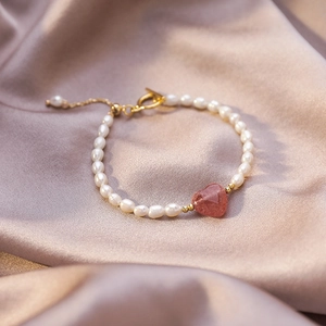 Detailed macro of baroque pearl bracelet featuring a red strawberry quartz heart and gold OT clasp