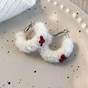 Vue détaillée de boucles d'oreilles en peluche blanche avec nœuds rouges sur assiette