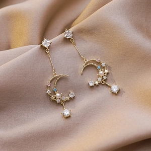 Macro shot of gold moon and star drop earrings with sparkling colorful zircons and pearls