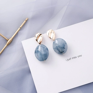 Detail view of blue marble dangle earrings with wavy gold metal links on a card
