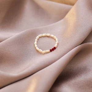Macro shot of handmade elastic ring featuring white freshwater pearls and red crystal beads