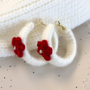 Détail de boucles d'oreilles créoles blanches tricotées avec fleur au crochet rouge et or
