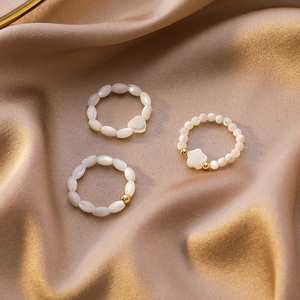 Close-up of beaded heart and flower rings on champagne satin fabric background