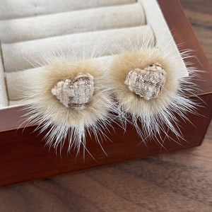 Détail des boucles d'oreilles cœur en tweed beige avec bordure en fausse fourrure douce