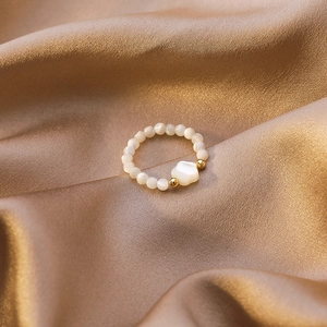 Macro shot of beaded shell heart ring on champagne silk fabric with gold accents