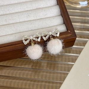 Détail de boucles d'oreilles boules beiges avec nœud en cristal et perle blanche