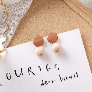 Détail d'une boucle d'oreille en résine caramel avec pompon crème et accents dorés