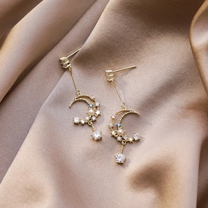 Detail of gold crescent moon earrings with blue zircons and trailing star tassels