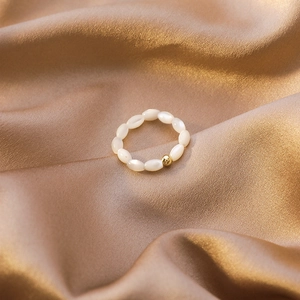 Elegant beaded ring featuring white oval shell pearls and a gold accent on silk fabric