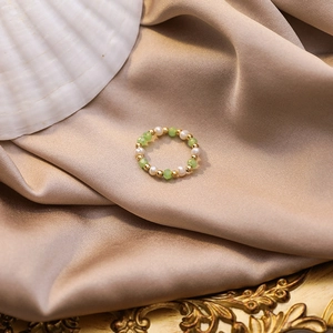 Detailed close-up of handmade beaded ring with freshwater pearls and green crystals