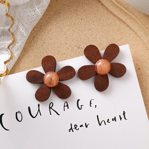 Détail de boucles d'oreilles fleurs en bois brun et résine marbrée sur fond de dentelle