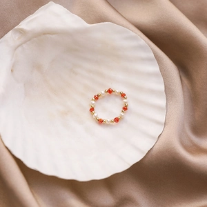Macro view of handmade beaded ring with red crystals and pearls on a white shell
