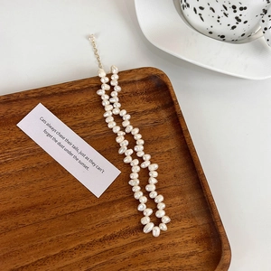 Gros plan d'un collier de perles d'eau douce baroques avec fermoir doré sur bois