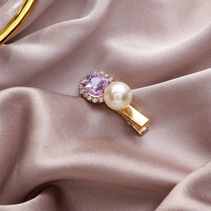 Close-up van gouden haarspeld met paarse edelsteen, witte parel en kristallen details