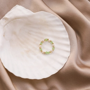 Detailed shot of handmade beaded ring with green crystal and pearls in a white seashell