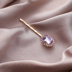 Detail van een gouden haarclip met rechthoekige paarse edelsteen en kleine diamanten