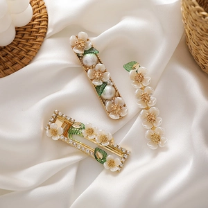 Three-piece floral hair clip set with white shell flowers and green leaves on gold base