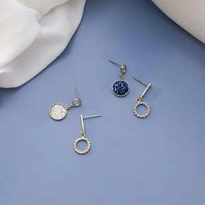 Detailed view of blue stardust cluster earrings and gold hoop dangles on light blue surface
