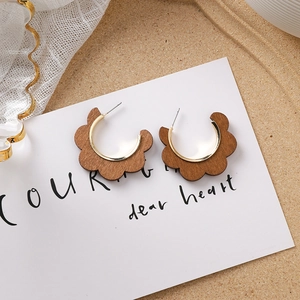 Détail de boucles d'oreilles en C avec métal doré et bords festonnés en bois brun