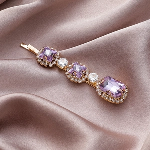 Elegante gouden haarklem met paarse steentjes en parels op roze zijden achtergrond