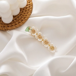 Detail of pearlescent flower hair clip with green leaf on white silk background