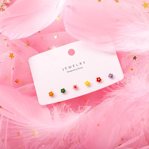 Detailed view of six colorful mini flower stud earrings on a jewelry card with pink feathers