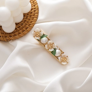 Detailed shot of rectangle hair clip with white resin flowers and green leaves on silk