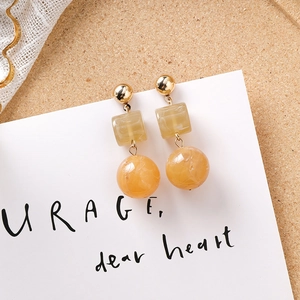 Détail de boucles d'oreilles géométriques en résine avec texture marbre jaune et perles dorées