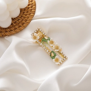 Detail of a floral gold hair clip with white shell flowers and green leaves on silk