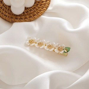 Detail of pearlescent flower hair clip with golden metallic base on white silk