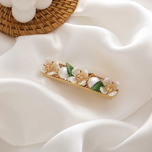 Detail of floral hair clip with white shell flowers, pearls and green leaves on gold base