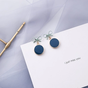 Detailed shot of elegant blue disc drop earrings featuring a green bow and enamel finish