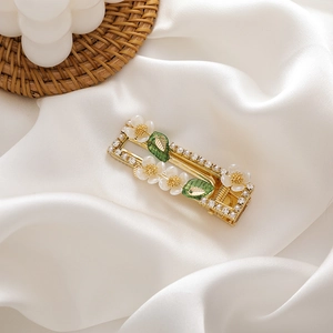 Detailed view of floral hair clip with white shell petals and green leaves on silk