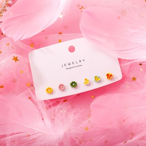 Detail of colorful daisy and butterfly earrings set on a dreamy pink feather background
