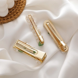 Detailed view of gold plated leaf and pearl hair clips on white silk background