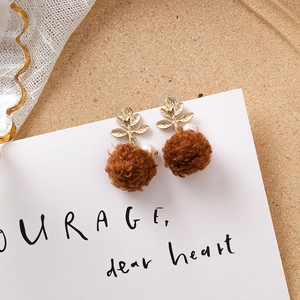 Détail de boucles d'oreilles boules en peluche brune avec feuille dorée et perle