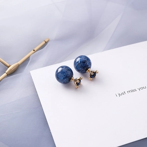 Close-up of blue spherical stud earrings with golden crown base and star-like texture