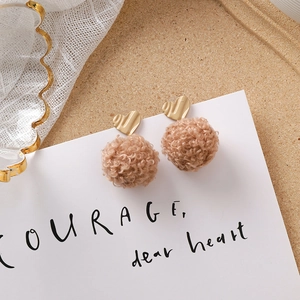Détail de boucles d'oreilles pompon kaki avec clous en métal texturé en cœur