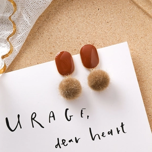 Détail de boucles d'oreilles en émail marron et pompon sur fond de dentelle rétro
