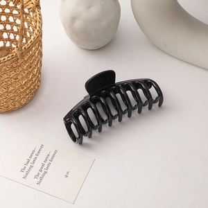 Close-up of a large glossy black hair claw clip with multi-tooth design on a minimal background